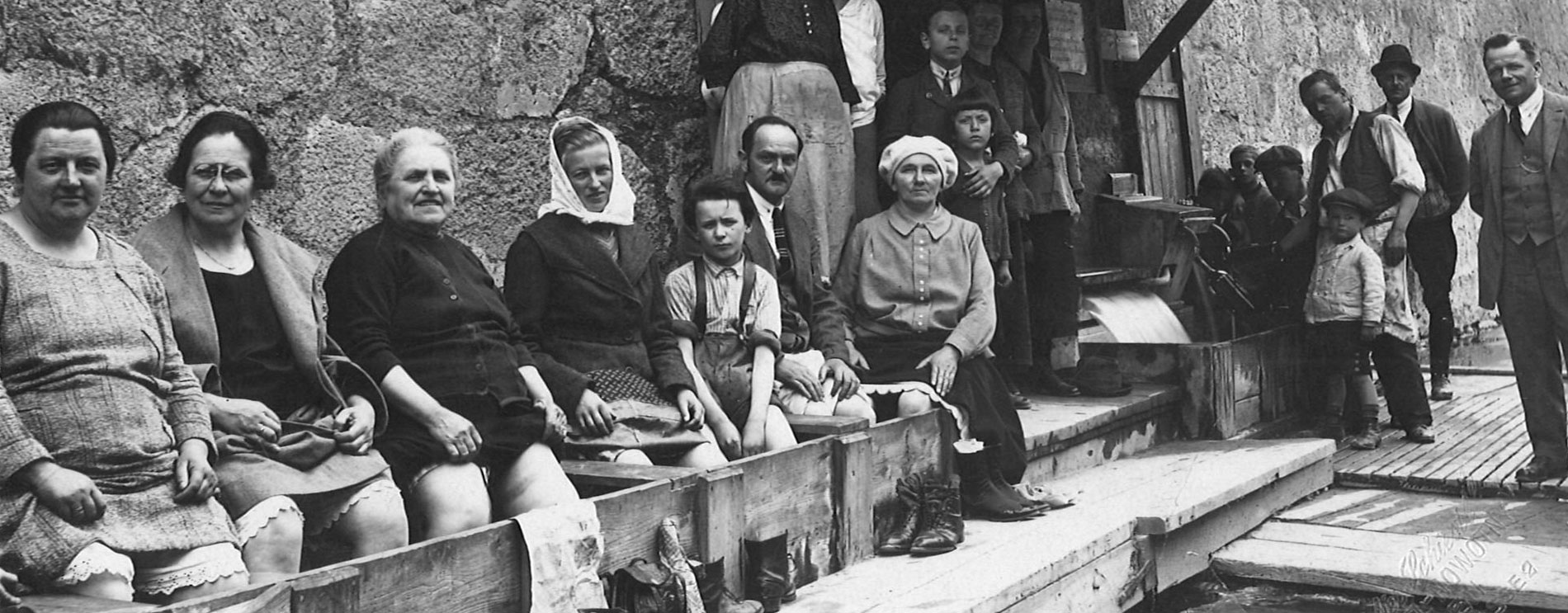Frauen sitzen vor einer Mauer und baden ihre Füße in einem Bretterverschlag; davor die Schwechat; Schwarzweißfoto.