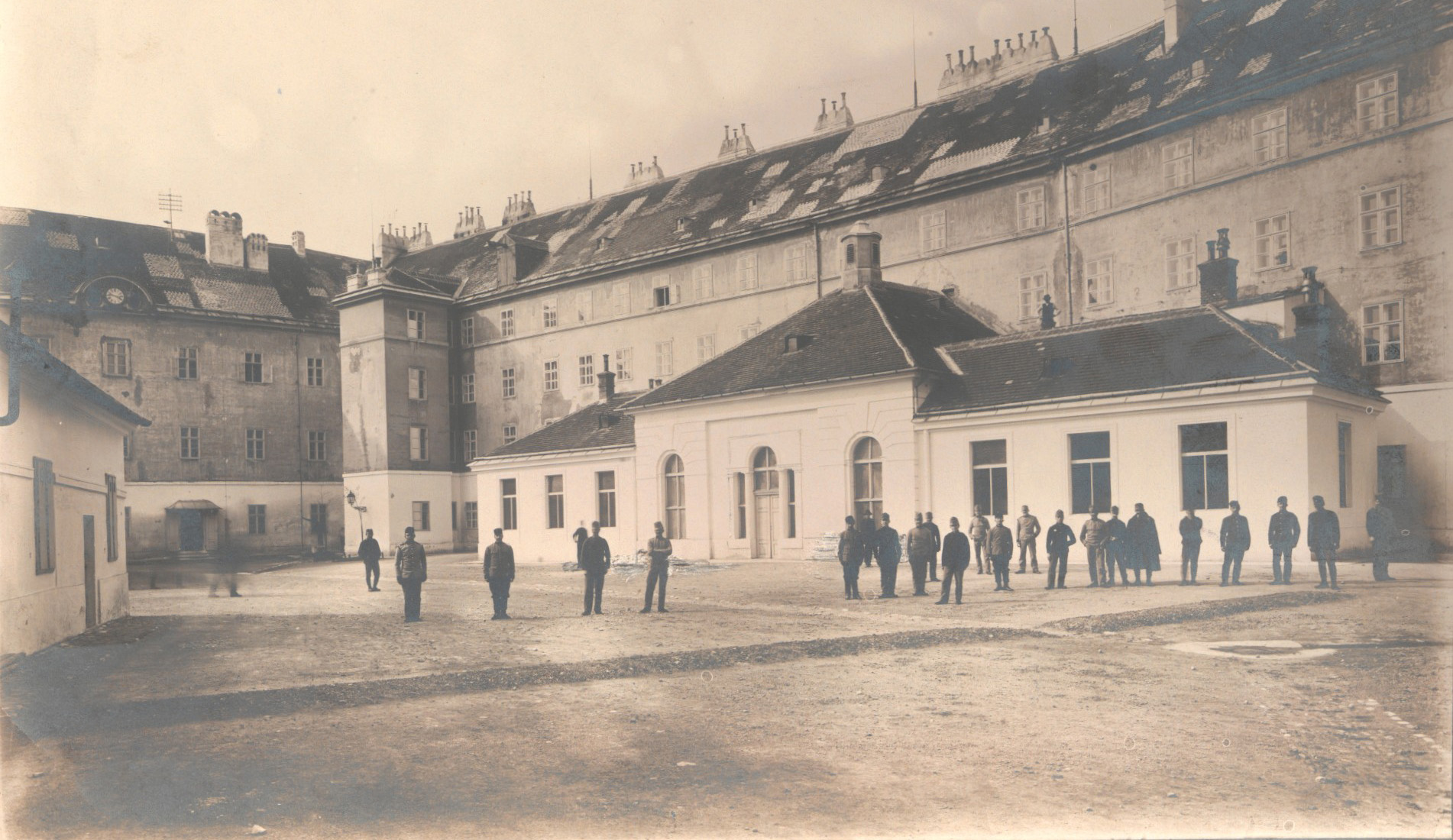 Einstöckiger rechteckiger Pavillon mit Seitenflügeln; in massives mehrgeschossiges Gebäude ohne Dekor; Schwarzweißfoto.