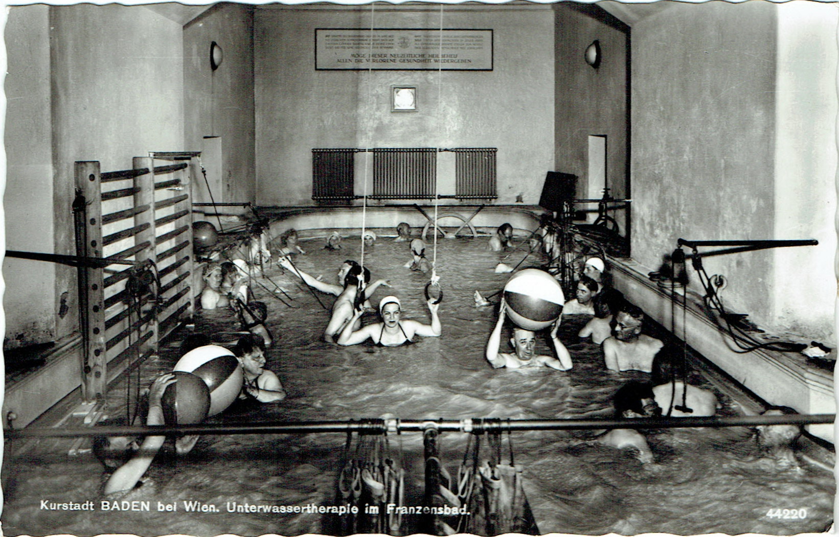 Baderaum mit Turngeräten; Ringe hängen von der Decke bis knapp über die Wasseroberfläche, mit Menschen.