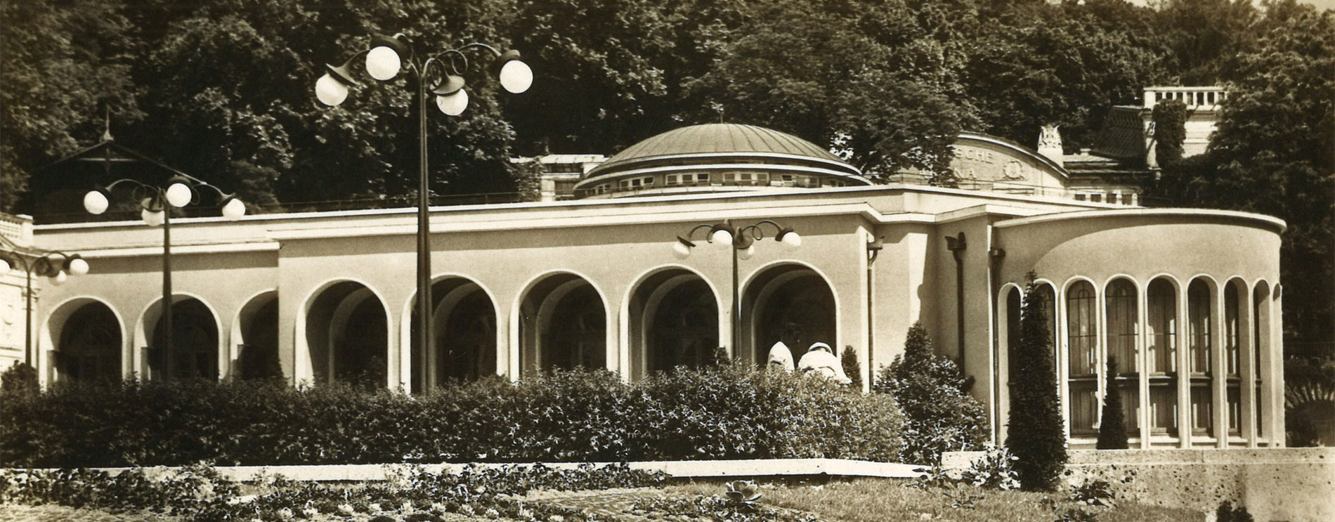 Blumenuhr; links hinten Gebäude mit Rundbogen; Schwarzweißfoto.