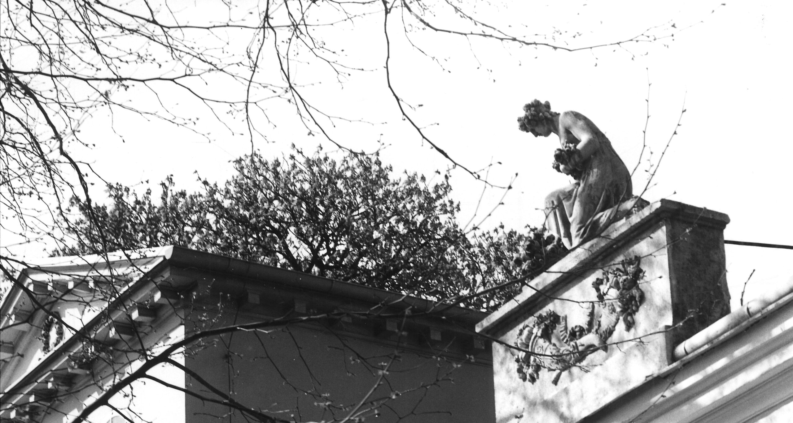 Schwarzweißfoto der Dachtraufe; kniende Flora-Steinfigur blickt nach links, darunter zwei Füllhörner in Relief.