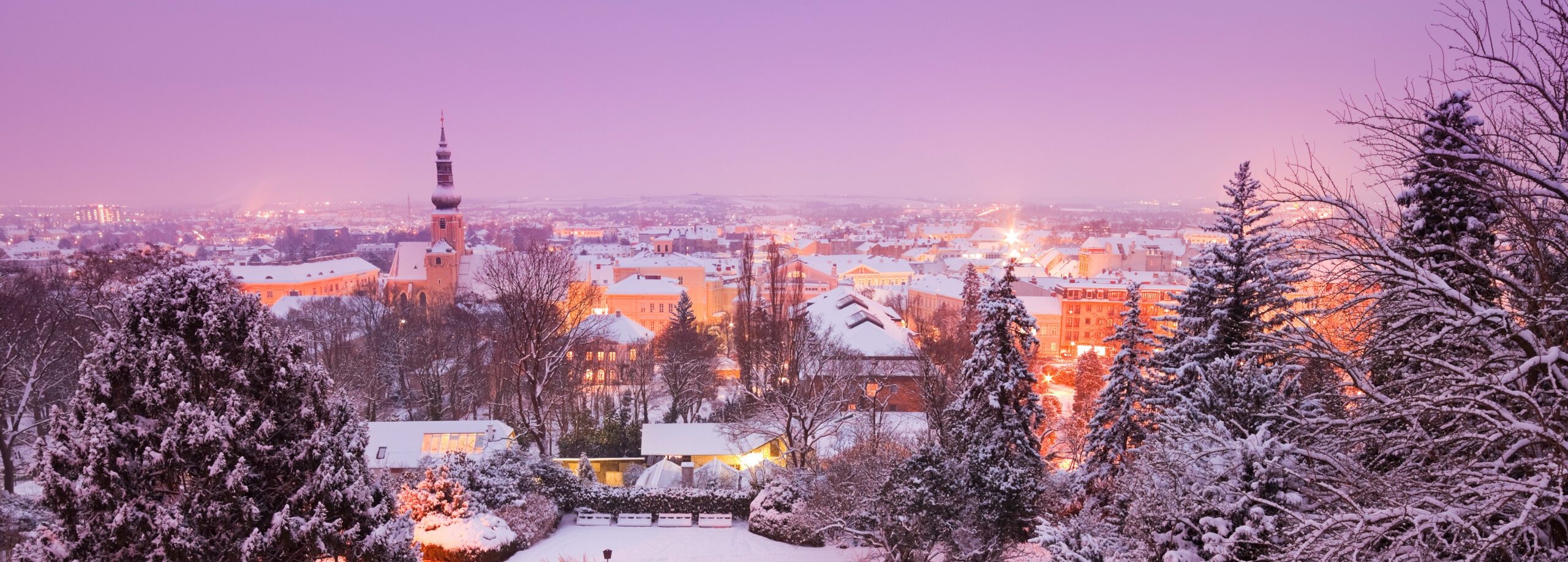 Blick vom verschneiten Kurpark auf Kirche und winterliche Dächer im Abendlicht.