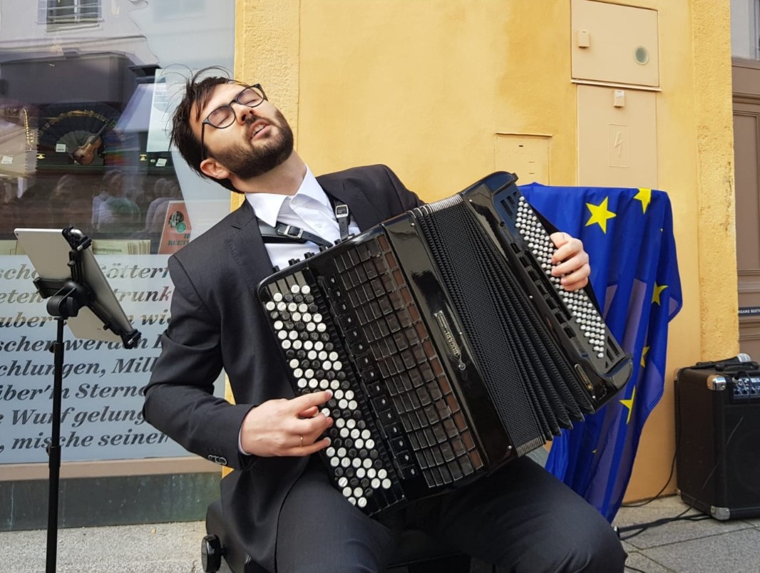 Musiker im Anzug, vertieft in sein Spiel; dahinter gelbe Fassade des Beethovenhaus Baden mit Europafahne.