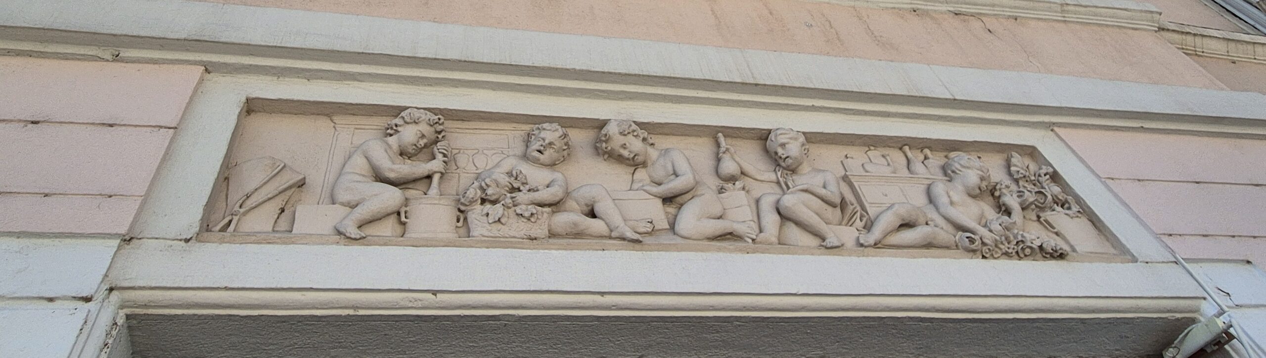 Relief aus Stein zeigt mehrere Figuren, die mit Mörser und Stößel arbeiten und etwas zusammenrühren.